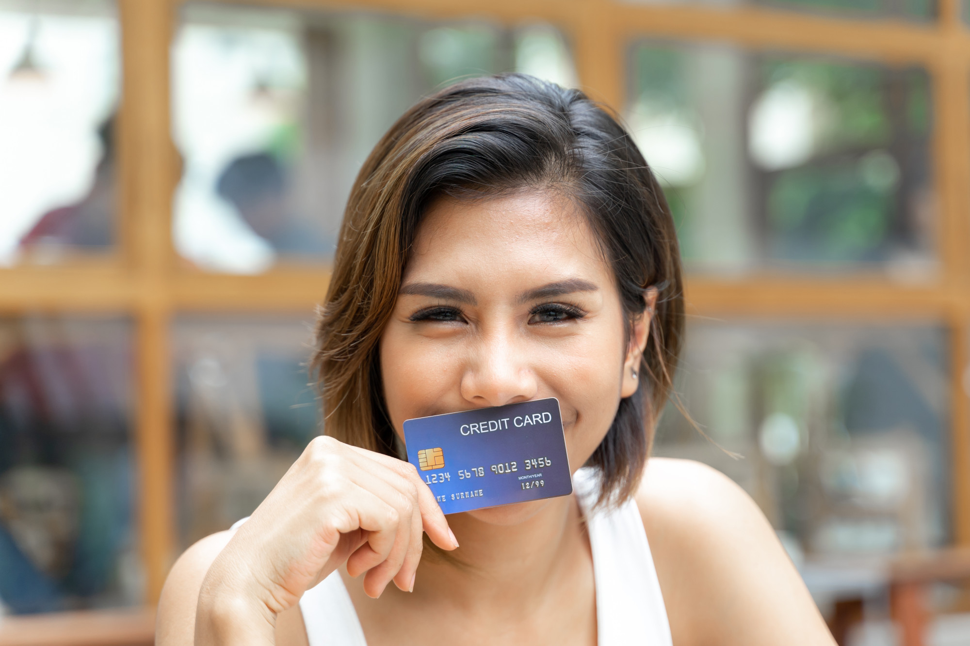 Mujer sonriendo mostrando su tarjeta de crédito sin anualidad ni comisiones.