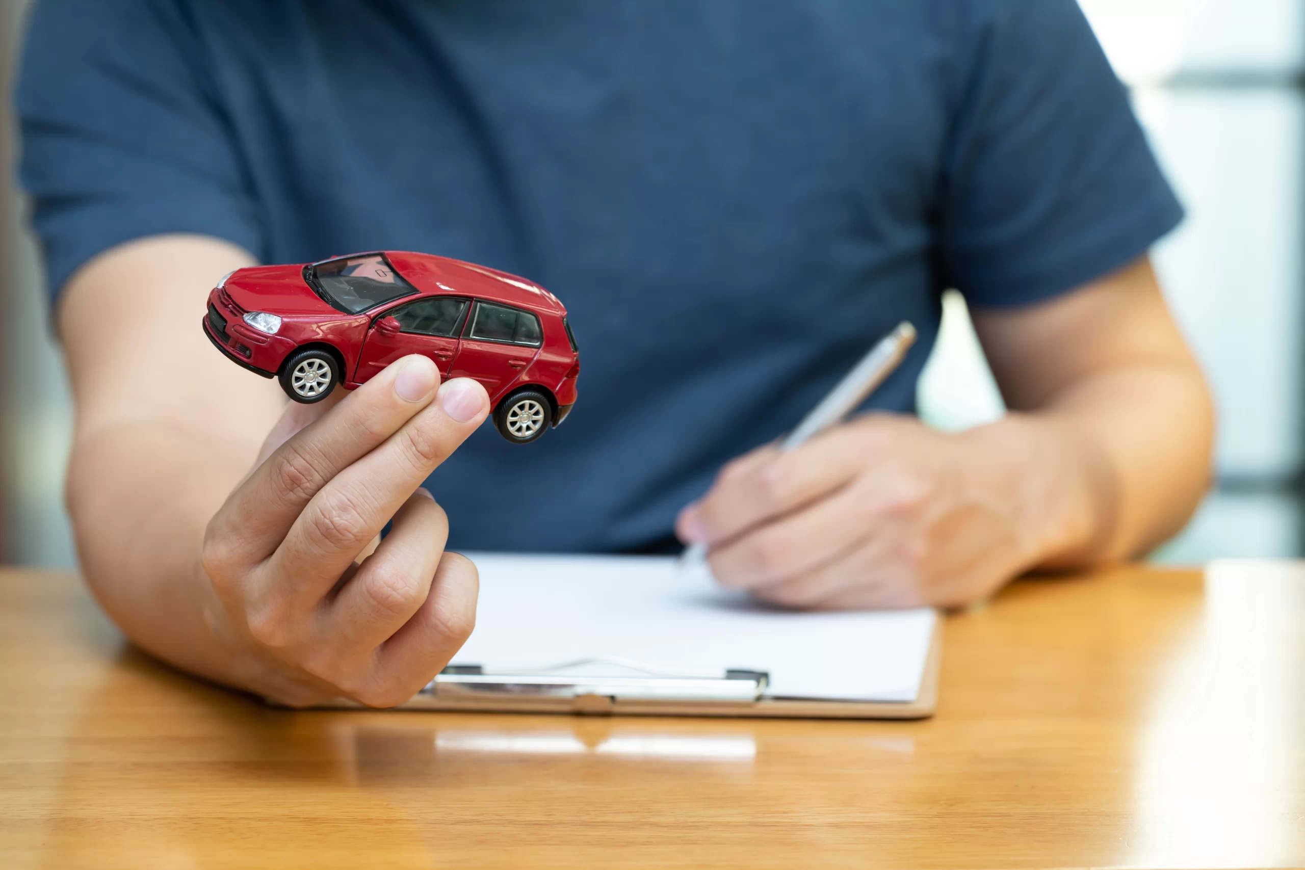 Hombre sosteniendo un auto de juguete mientras contrata un seguro de auto Scotiabank.