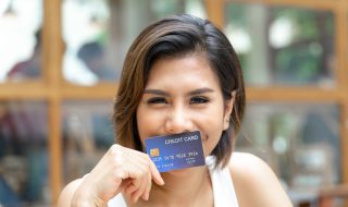 Mujer sonriendo mostrando su tarjeta de crédito sin anualidad ni comisiones.