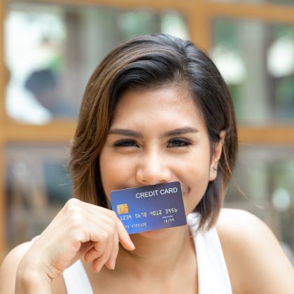 Mujer sonriendo mostrando su tarjeta de crédito sin anualidad ni comisiones.
