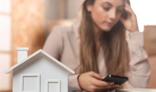 joven mujer junto a casa de madera aprendiendo cómo evitar fraudes con créditos hipotecarios.