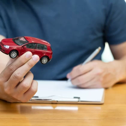 Hombre sosteniendo un auto de juguete mientras contrata un seguro de auto Scotiabank.